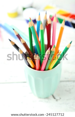 Colorful pencils in cup on white wooden background
