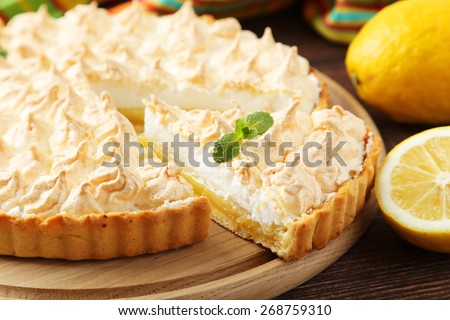 Lemon meringue pie on cutting board on brown wooden background
