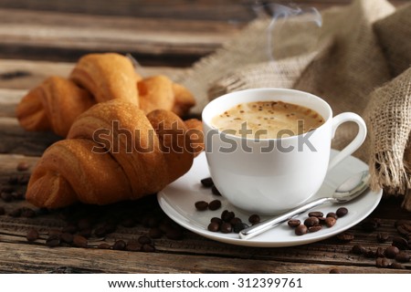 Delicious croissants with cup of coffee on brown wooden background