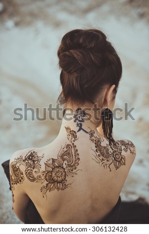 Drawing mehndi by means of henna on hands and a back of the girl.