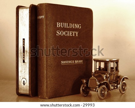 Miniature car standing beside two money boxes in the form of books.  Represents concept of \'Saving for the real thing\'