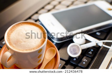 Coffee cup with smart phone and headphones on laptop.