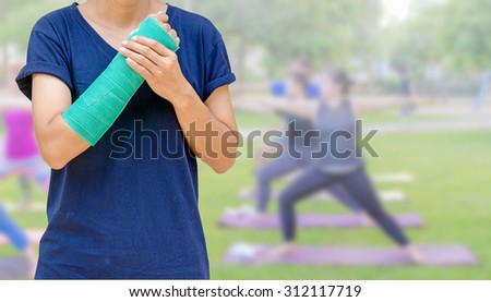 broken arm with green cast on blurred woman fitness group - yoga team, insurance concept