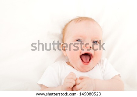 happy smiling child with blue eyes lying in bed over white