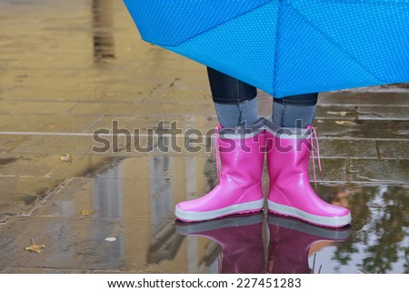 Person with pink boots and blue umbrella standing in a puddle