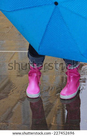 Person with pink boots and blue umbrella standing in a puddle