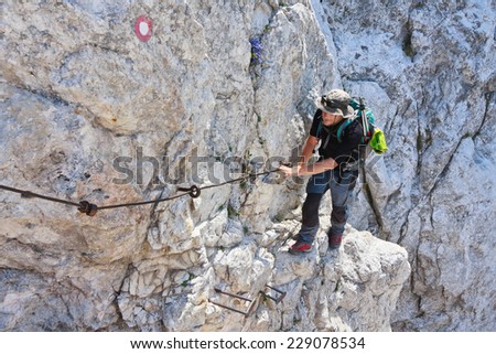 Mountaineer climbing the rocky slovenska pot wall on a path to Kepa mountain secured by pins and cables, Slovenia