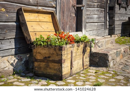 Old wooden box with open lid with blooming flowers based on the wooden building.
