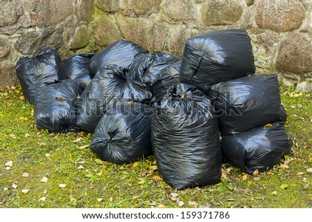 Full black plastic bag in park in the background of stone wall.