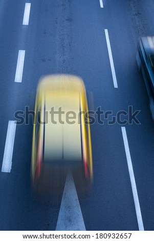 A blurred yellow car, speeding on the city road, white road lines.
