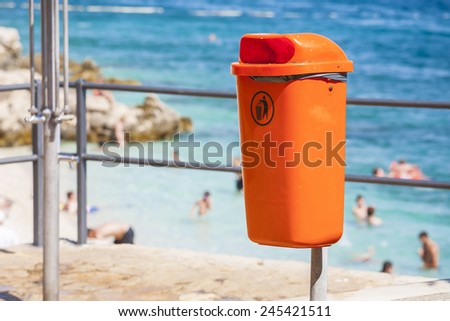 Orange trash bin near the sea beach. Littering the beach and the sea.