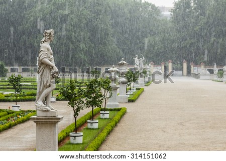 Park in the pouring rain. Alley in baroque park in the rain. Space for text.  Sculpture by Chrysostom Redler eighteenth century sculptor.