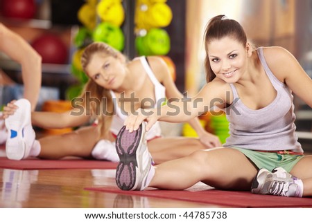 Two smiling girls do exercise in sports club