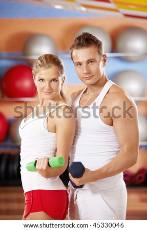 Two beautiful trainers with dumbbells in hands in sports club