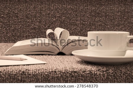 Pages of open book rolled in heart shape with coffee on table.