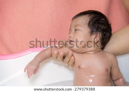 newborn baby taking a bath by mother at home, asian child.