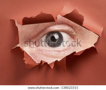 Man\'s eye spying through hole in paper