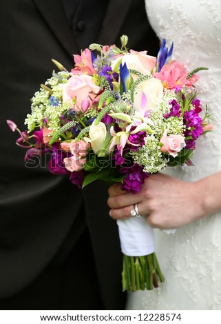 Bride holding wedding bouquet flowers against groom