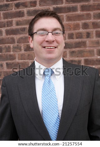 Smiling young urban businessman in front of brick wall