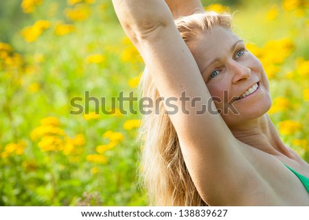 tight shot of Caucasian blonde middle-aged woman arms stretched high in the middle of a meadow of yellow ragweed flowers.  Blue Hill, Maine, Summer