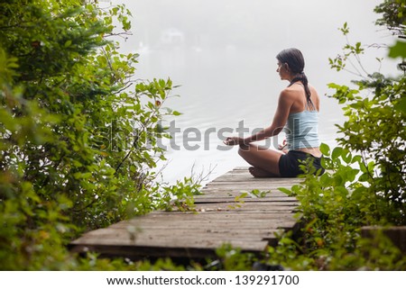 middle aged woman meditating on dock by a lake in the foggy morning, horizontal composition, Surry Maine
