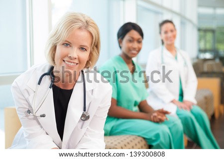 Female caucasian doctor sitting on couch with African-American nurse and hispanic nurse in hospital waiting area or lobby
