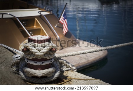 The yacht with the US flag docked at a pier. Selective focus on mooring bollard with nautical rope knotted on it.