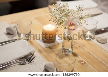 Birthday reception table setting with flowers and candles with flame. Shooting in poor conditions with high ISO. Developed from RAW; retouched with special care and attention;