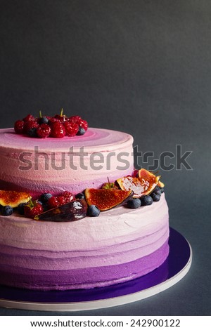 Two tiered purple cream cake with fruit on dark gray background