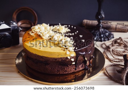 Chocolate cake with flowers and mango mousse on dark vintage rustic background with retro camera and decorations