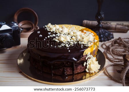 Chocolate cake with flowers and mango mousse on dark vintage rusic background with retro camera and \
decorations