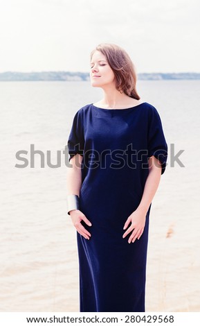 Young beautiful woman in long navy blue dress on summer beach near water
