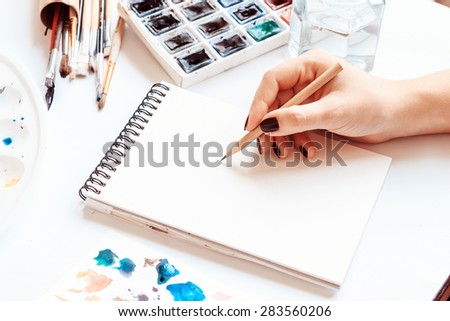 Human hands with pencil draws in notebook. Drawing accessories around