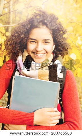 Female student in warm autumn. A smiling Latino American young girl with books in hand on the background of the autumn landscape.