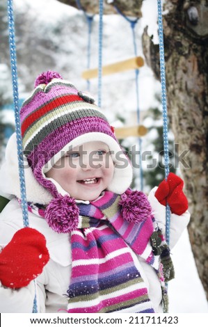 Happy Little girl in a winter garden. Pretty little girl sitting on a swing in the winter.