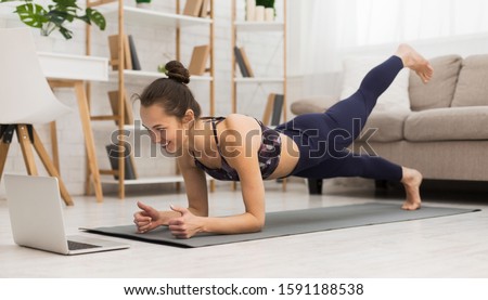 Fit woman doing yoga plank and watching online tutorials on laptop, training in living room Stock fotó © 