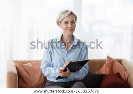 Professional Psychotherapy. Successful Psychologist Holding Folder Smiling To Camera Sitting On Sofa In Office.