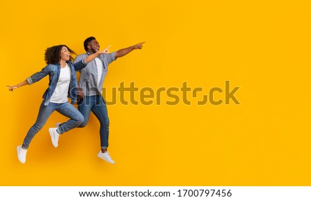 Great Offer. Positive black couple jumping in air and pointing at copy space on yellow background, panorama 商業照片 © 