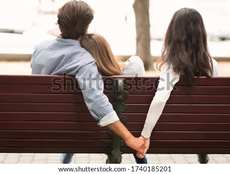 Love Triangle. Cheating Boyfriend Hugging Girlfriend Holding Hands With Her Girl Friend Sitting On Bench Together In Park Outdoor. Back-View Stock foto © 