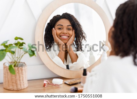 Self-Care. Beautiful African American Woman In Bathrobe Ready To Apply Makeup, Reflecting In Mirror Of Toilette Dresser Table, Looking At Camera