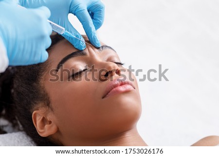 Plastic surgery. Young african woman receiving botox injection in interbrow zone at beauty clinic, closeup, copy space