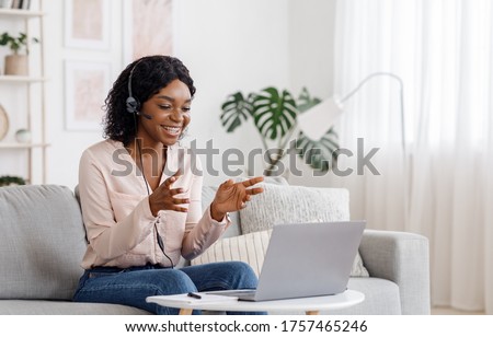 Photo of Video Conference. Smiling african woman having web call on laptop at home, talking at camera while sitting on sofa in living room