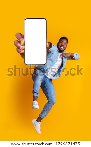 Advertisement for mobile application. Excited african guy dancing over yellow background, showing modern smartphone with empty screen, collage
