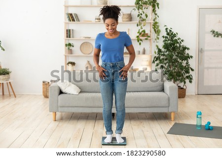 Weight-Loss Motivation. Smiling African Woman Weighing Herself After Successful Slimming And Weight Loss Standing On Scales Posing At Home. Full Length, Free Space For Text Photo stock © 