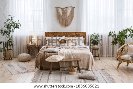 Rustic home design with ethnic decoration. Bed with pillows, wooden furniture, plants in pots, armchair and curtains on large windows in cozy bedroom interior, nobody, flat lay, panorama, free space