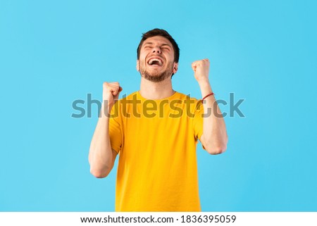 Winner Concept. Studio portrait of young man yelling with clenched fists raised up in the air, isolated over blue background. Excited guy cheering and screaming, celebrating victory Foto stock © 