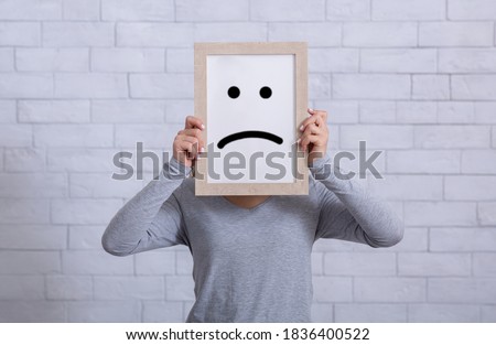 Depression, sadness, negative emotions concept. Young woman holding picture frame with sad emoticon in front of her face. Millennial lady expressing pessimism, loneliness, grief or frustration ストックフォト © 