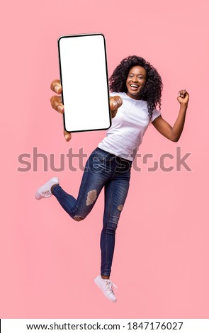 Excited black lady holding smartphone, showing blank screen, jumping up over pink studio background. Attractive african american young woman recommending new mobile application, collage