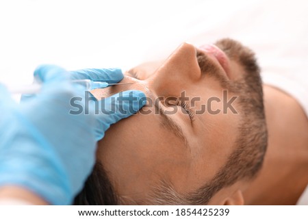 Closeup of bearded man getting beauty injection in clinic. Cosmetologist hands in blue rubber gloves doing face filling procedure for handsome man. Face care, male cosmetology concept Foto stock © 