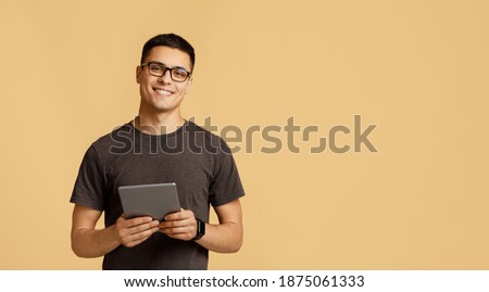 Teacher, tutor, blogger or student. Cheerful young attractive man in glasses looks at camera, holds digital tablet on online lesson, isolated on light background, panorama, empty space, studio shot